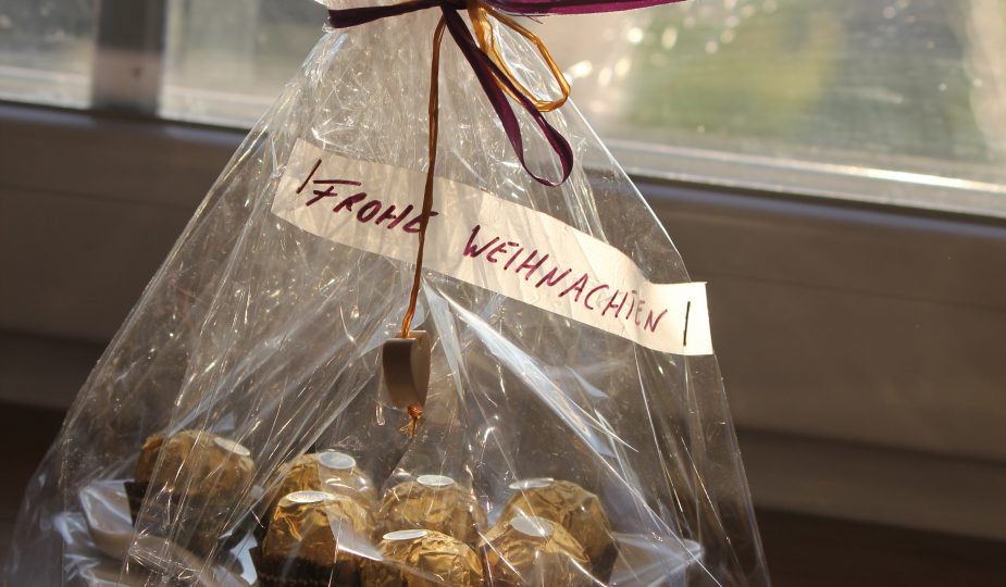 Christbaumteller mit Ferrero Rochers belegt liegt auf einer Packung Weihnachtsservietten. Das ganze ist in Zellophan mit Herzanhänger verpackt.