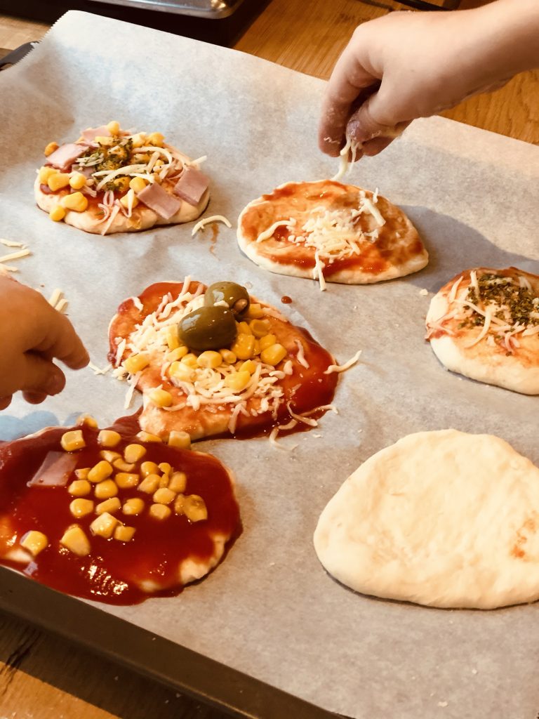 Kinderhände beim belegen der Pizzabrötchen.