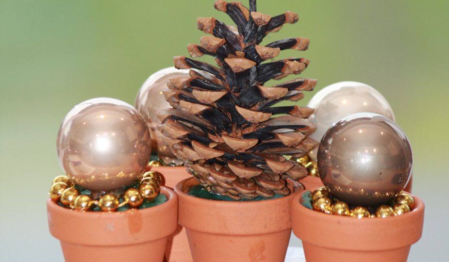 Mini-Blumentöpfe mit kleinen Christbaumkugeln oder Tannenzapfen geschmückt.